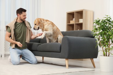 Cute Labrador Retriever giving paw to happy man at home. Space for text