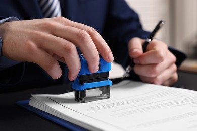 Photo of Notary with pen stamping document at table in office, closeup