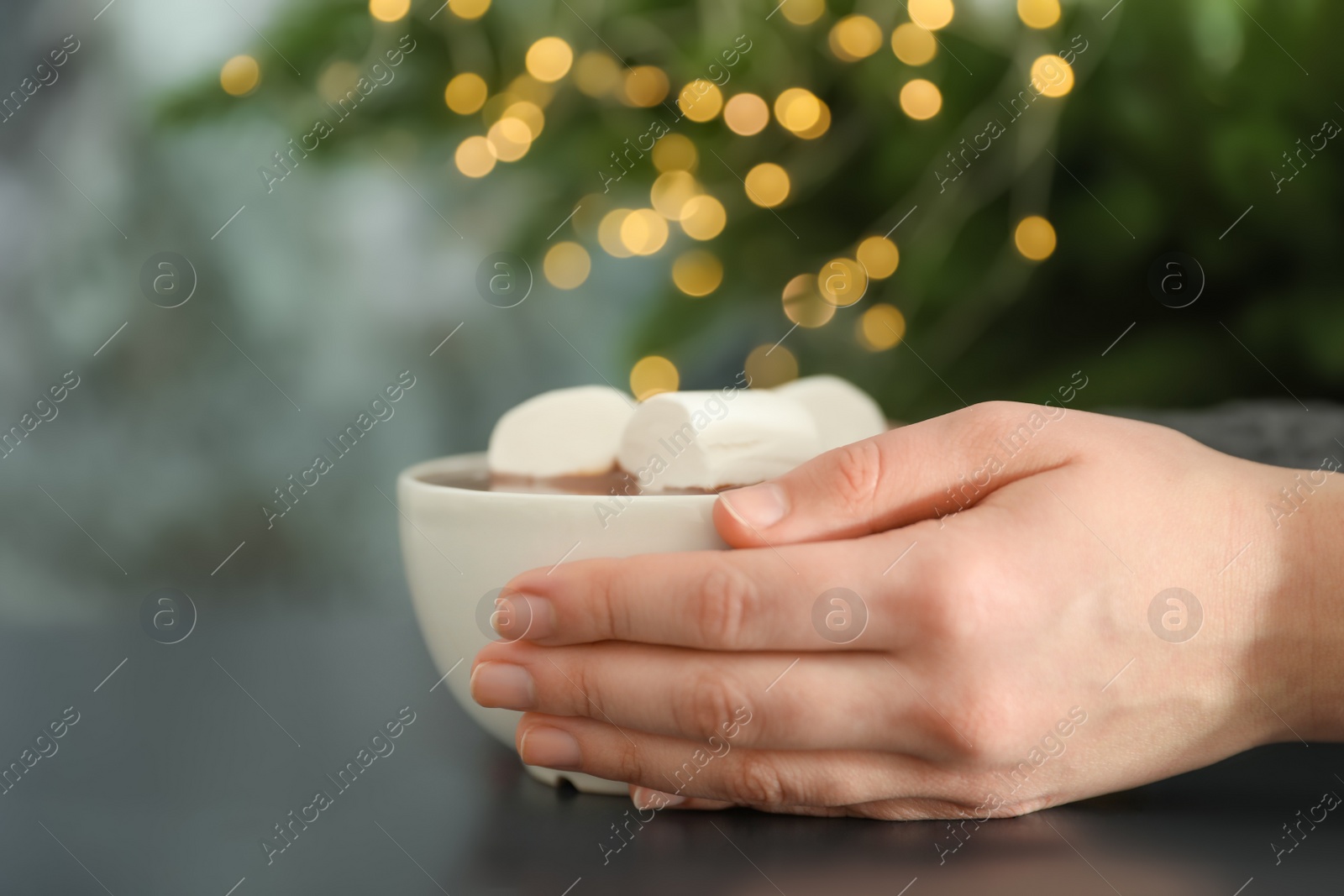 Photo of Woman holding cup of aromatic cacao with marshmallows on table, closeup. Space for text