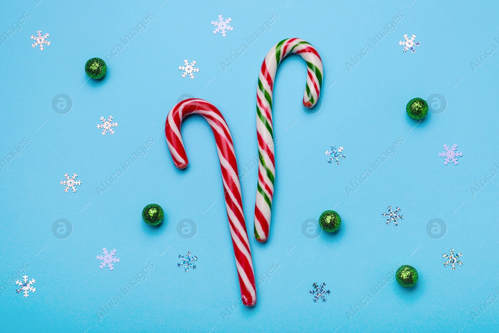 Photo of Flat lay composition with sweet Christmas candy canes and festive decor on light blue background