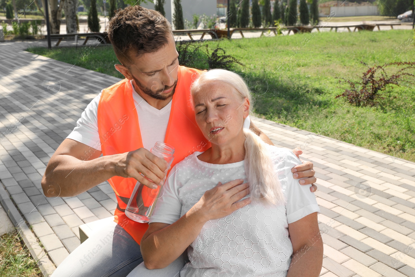 Photo of Worker with bottle of water helping mature woman on city street. Suffering from heat stroke