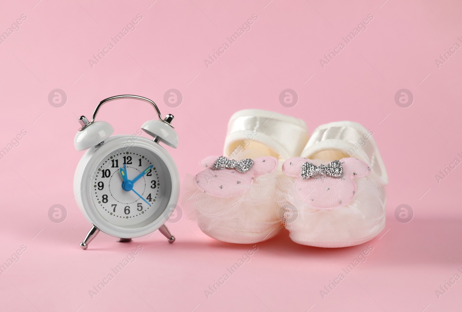 Photo of Alarm clock and baby booties on pink background. Time to give birth