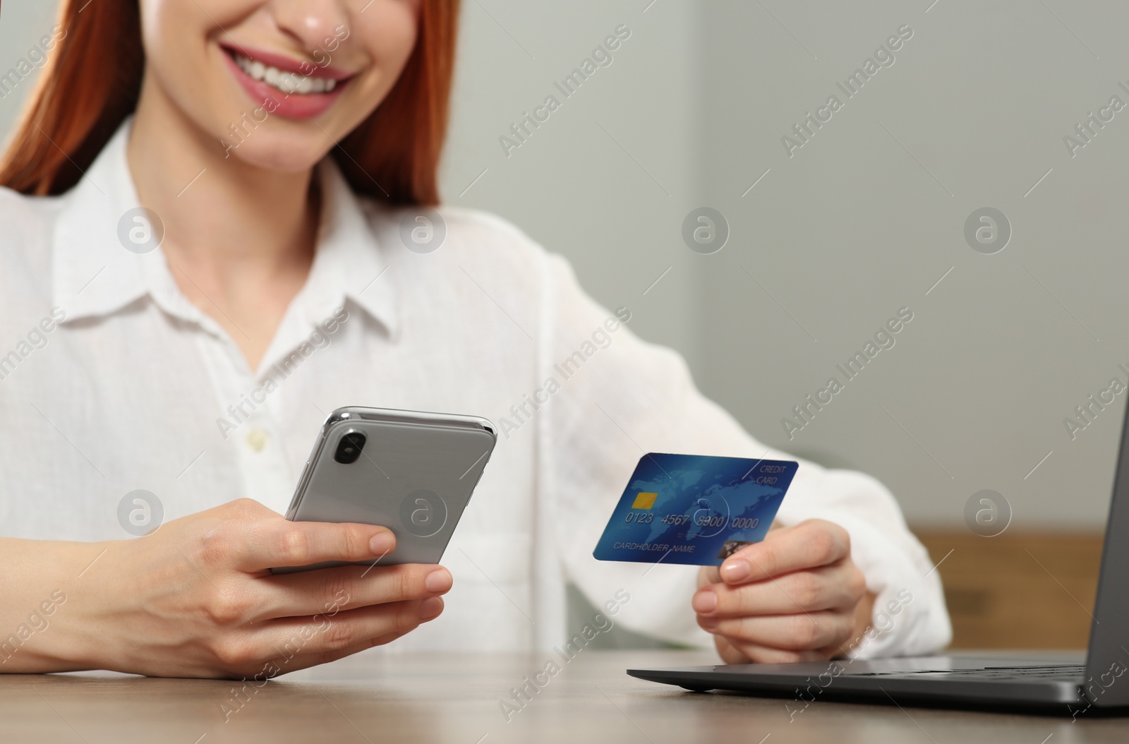 Photo of Woman with credit card using smartphone for online shopping at wooden table indoors, closeup