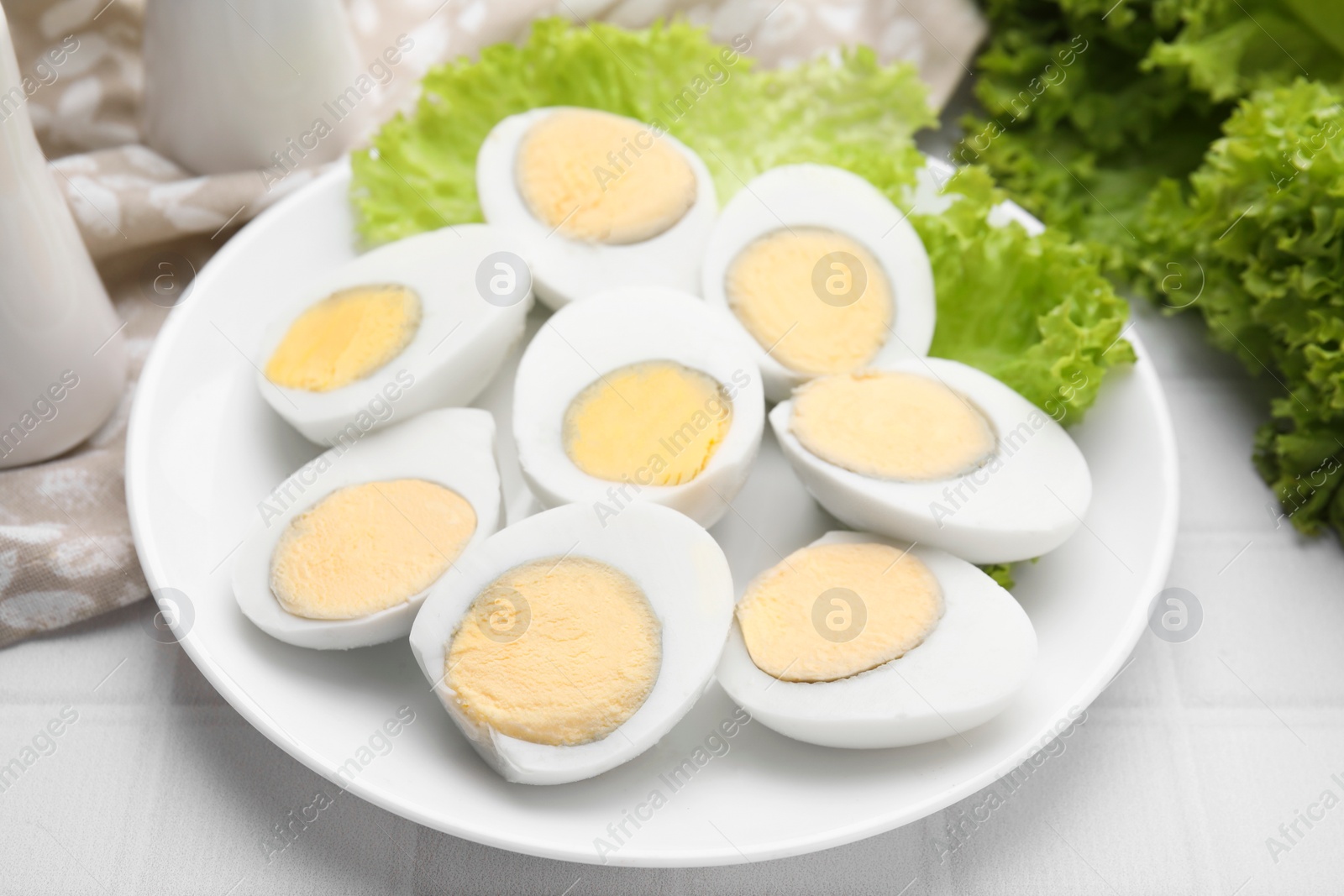 Photo of Fresh hard boiled eggs and lettuce on white tiled table