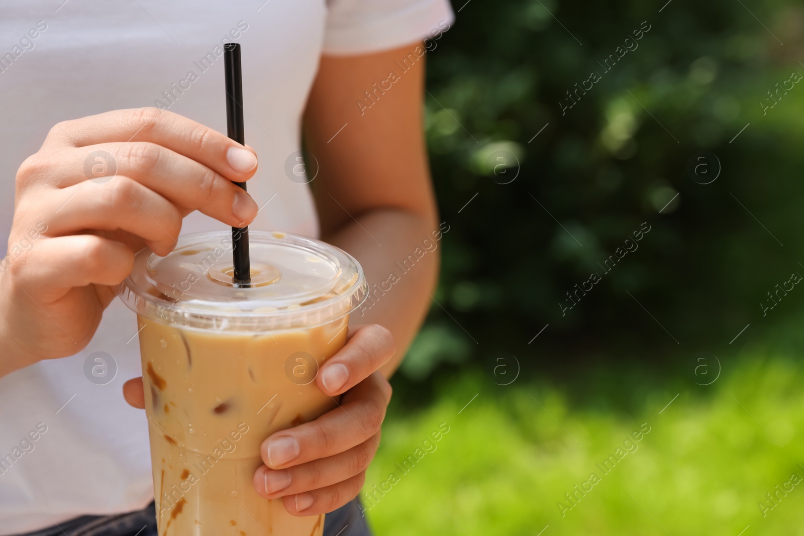 Photo of Woman holding takeaway plastic cup with cold coffee drink outdoors, closeup. Space for text