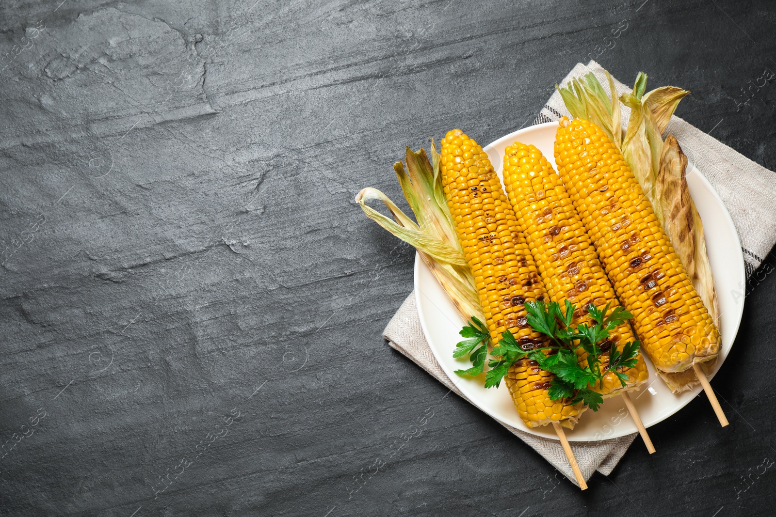 Photo of Tasty grilled corn on black table, space for text