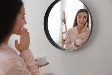 Photo of Young woman applying face cream at home. Morning routine