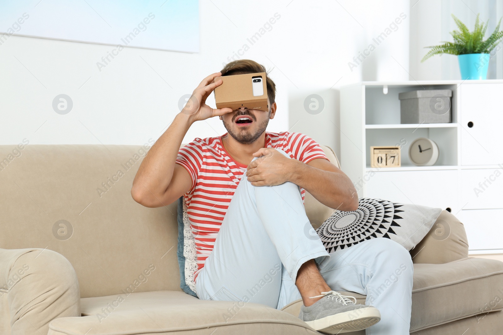 Photo of Young man using cardboard virtual reality headset at home