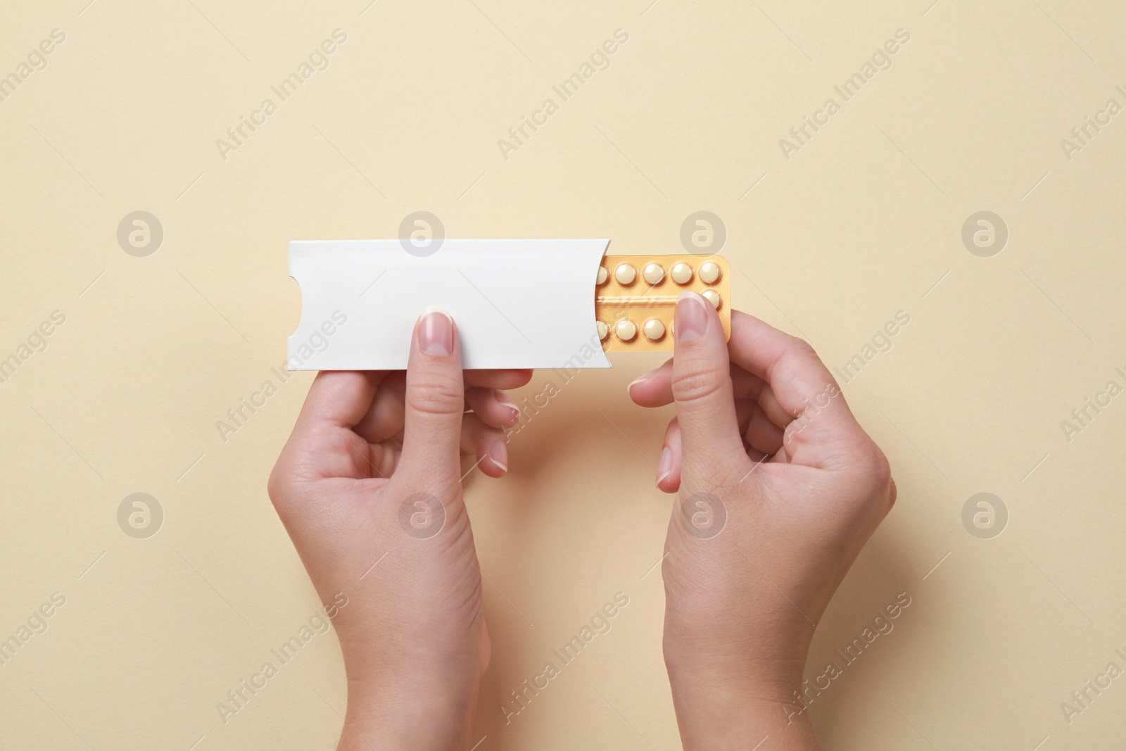 Photo of Woman holding blister with birth control pills on beige background, top view