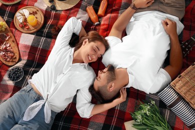 Happy young couple resting on picnic plaid, above view