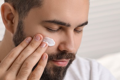 Man with dry skin applying cream onto his face on light background