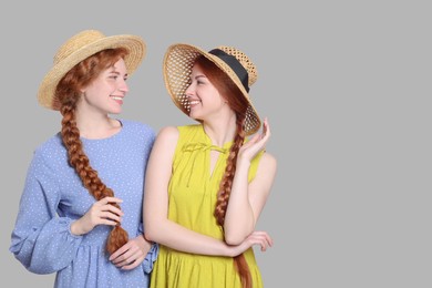 Portrait of beautiful young redhead sisters in straw hats on pink background. Space for text