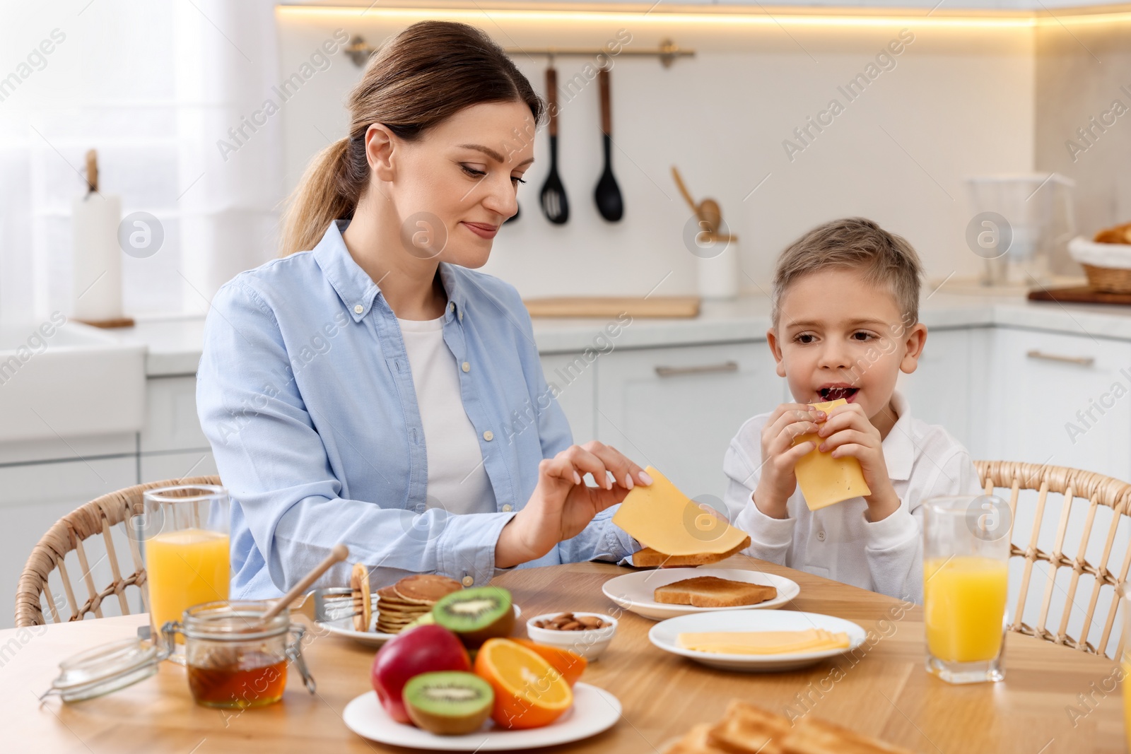 Photo of Mother and her cute little son having breakfast at table in kitchen