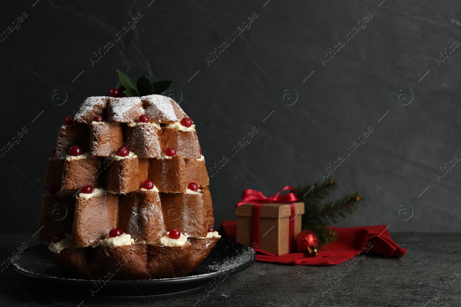 Photo of Delicious Pandoro Christmas tree cake with powdered sugar and berries near festive decor on black table. Space for text