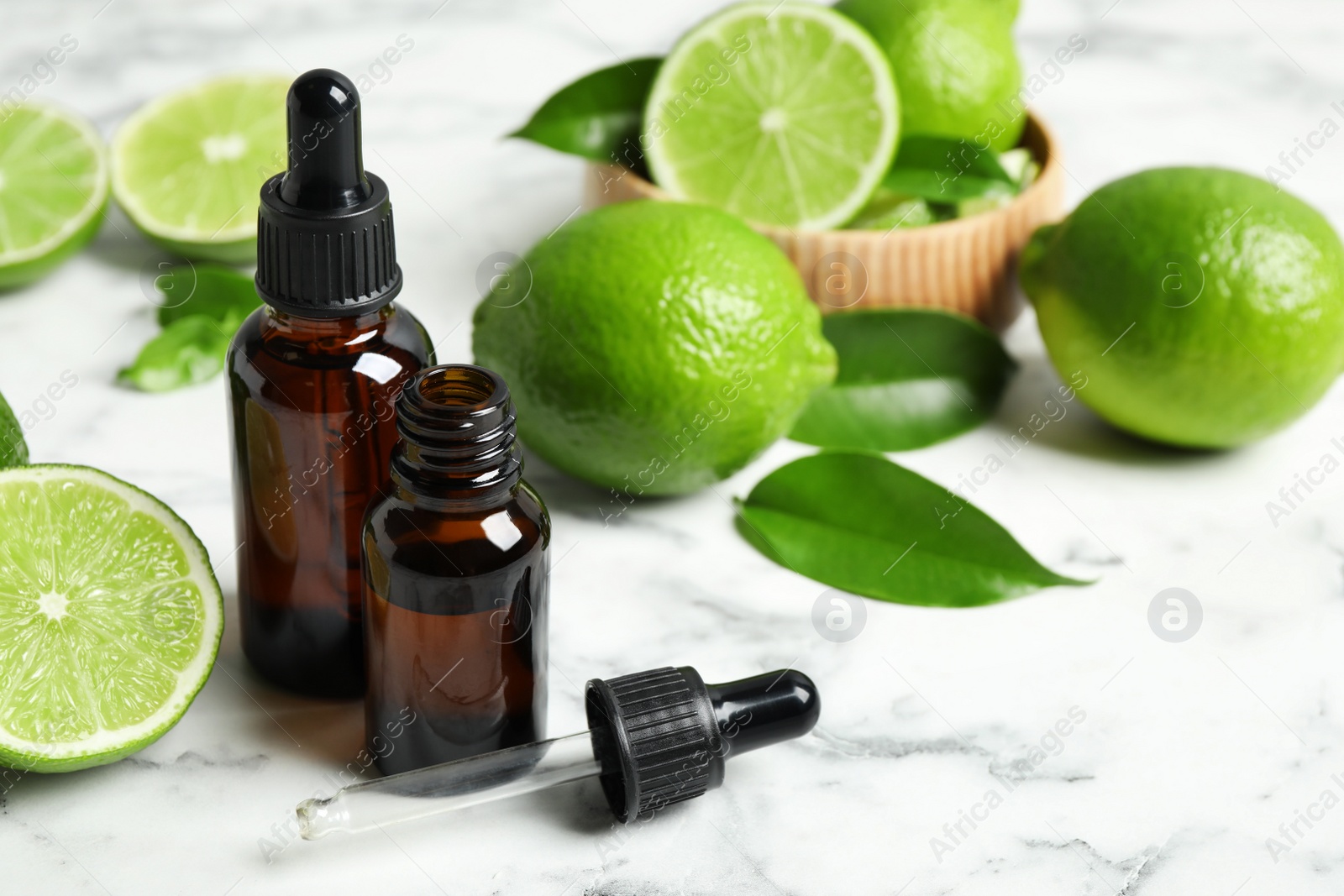 Photo of Lime essential oil and citrus fruits on marble table