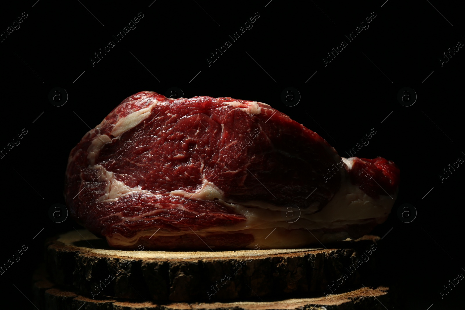 Photo of Piece of raw beef meat on decorative wooden stand against black background, closeup