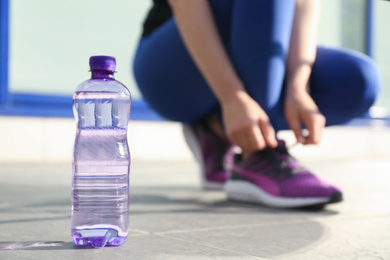 Photo of Plastic bottle of pure water and athletic woman outdoors, closeup