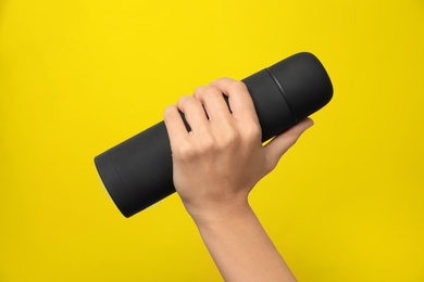 Woman holding modern black thermos on yellow background, closeup