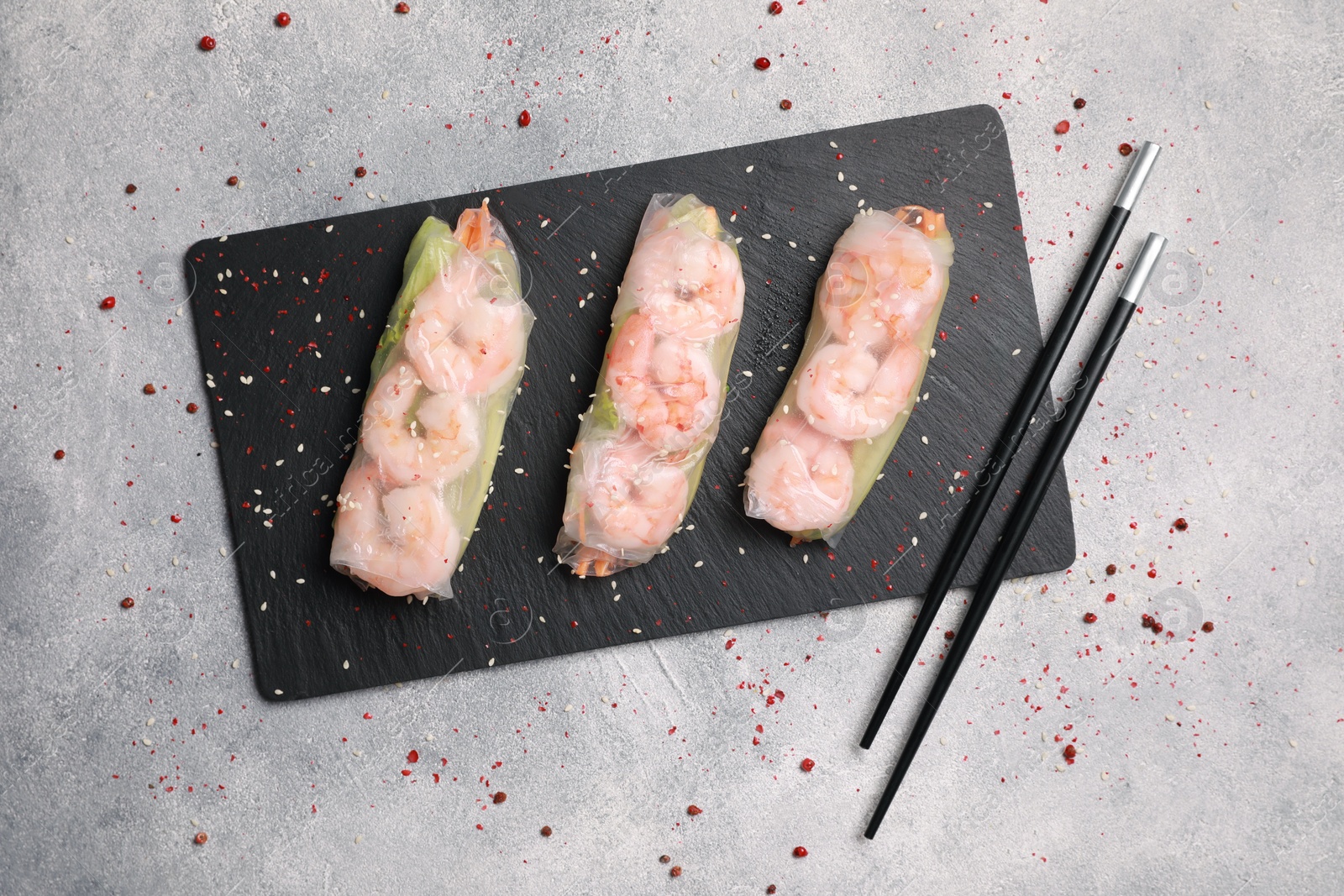 Photo of Tasty spring rolls served with spices on grey textured table, flat lay