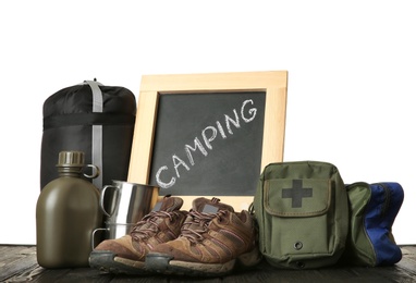 Photo of Set with different camping equipment and chalkboard on wooden table against white background