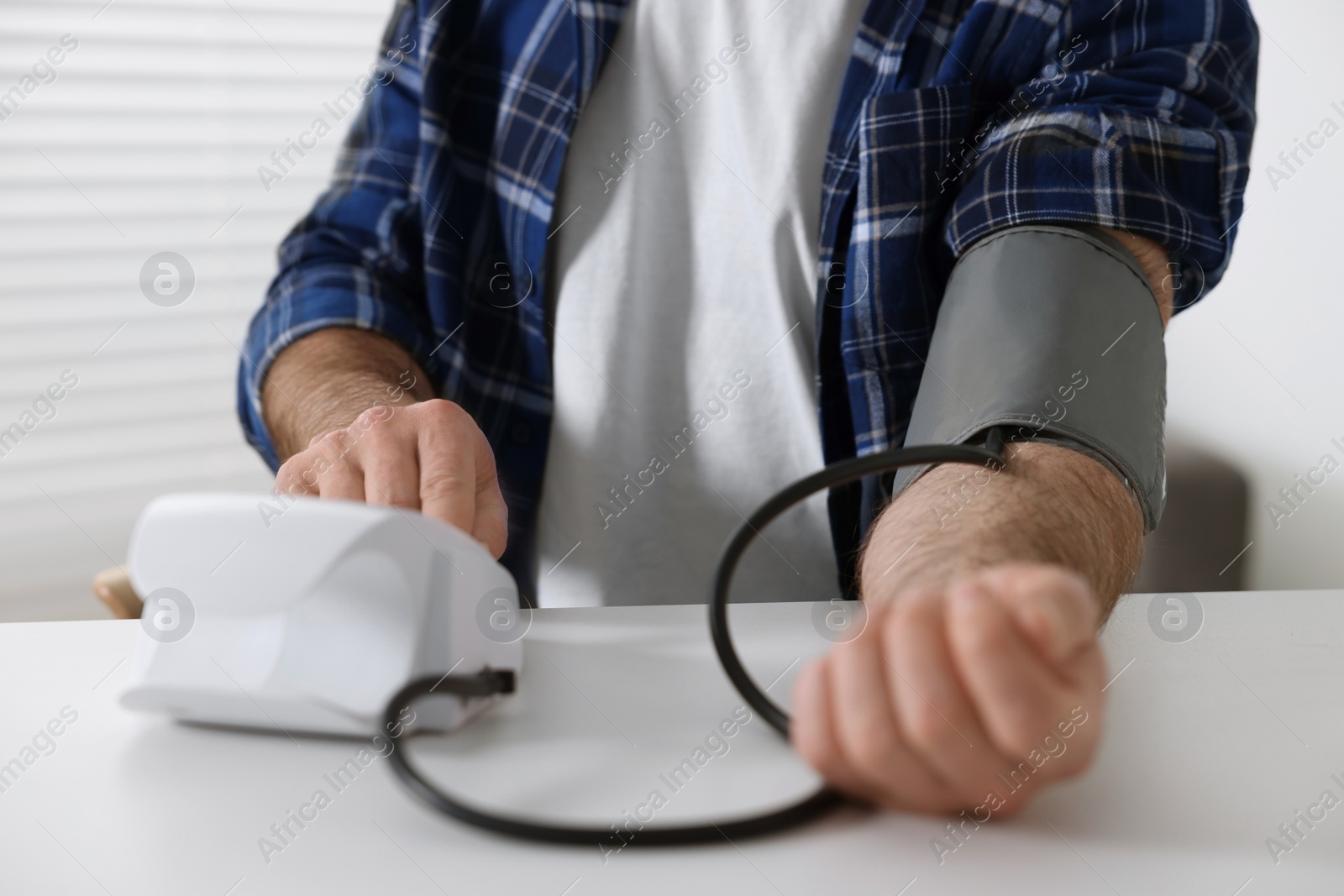 Photo of Man measuring blood pressure at table indoors, closeup