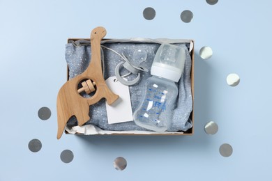 Different baby accessories with blank card in box and confetti on light blue background, top view