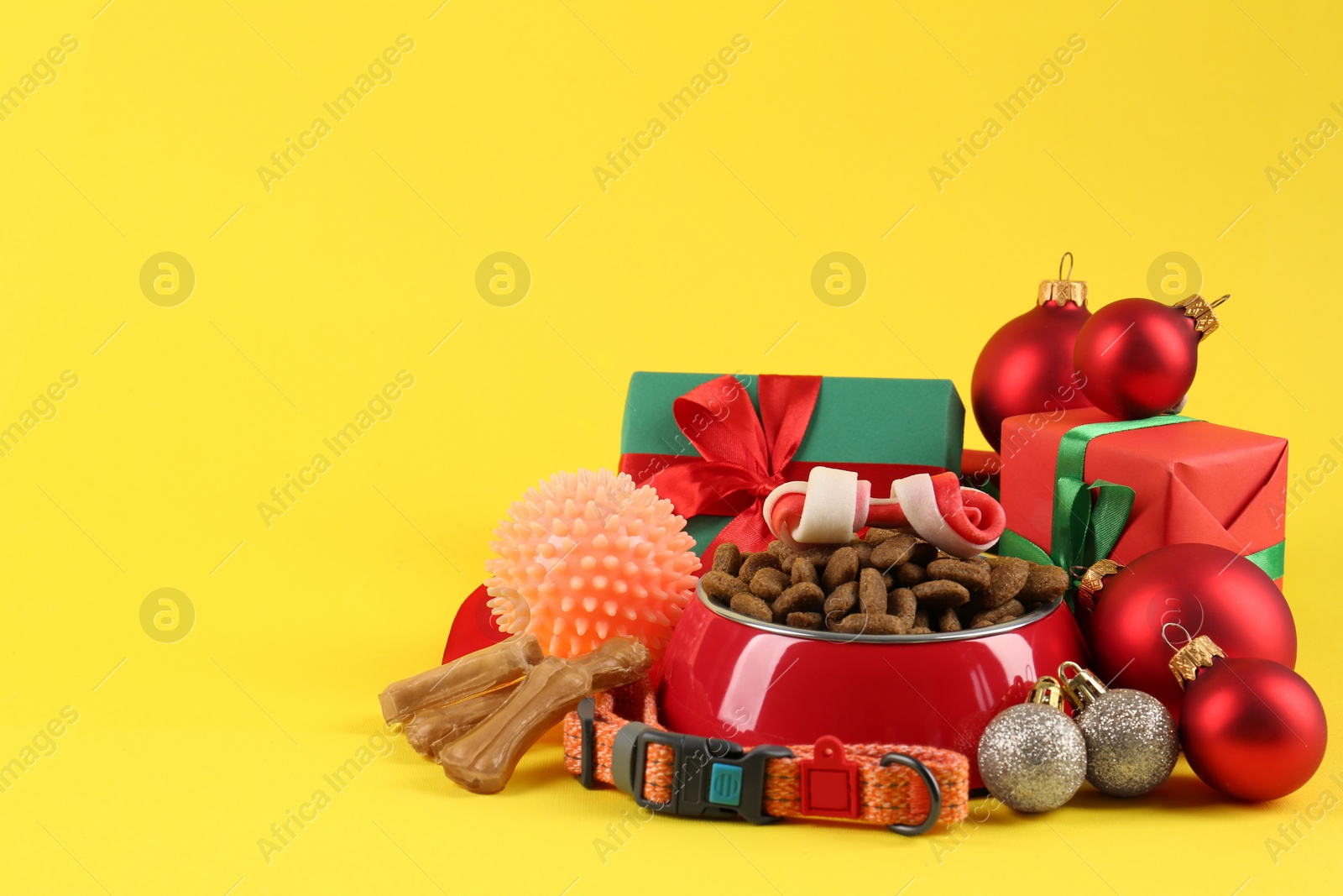 Photo of Different pet goods with Christmas gifts on yellow background, space for text. Shop assortment