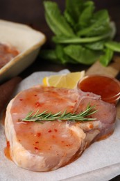 Photo of Raw marinated meat and rosemary on parchment, closeup