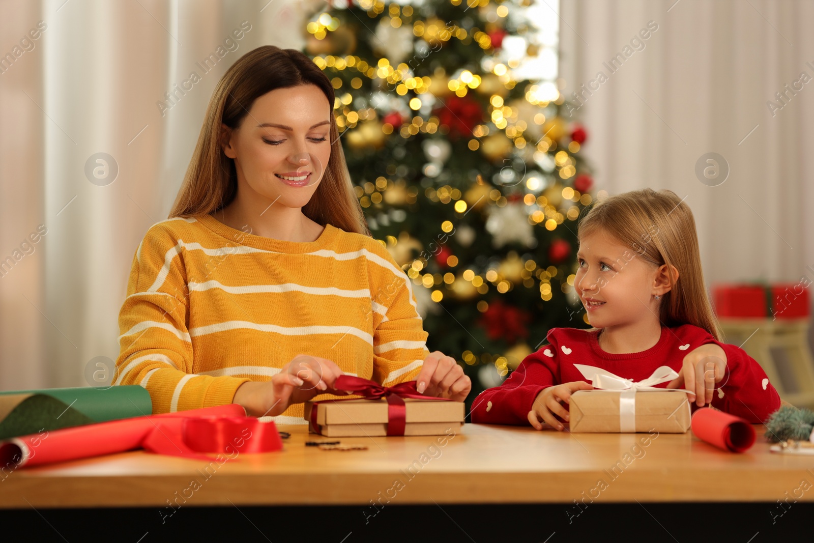 Photo of Christmas presents wrapping. Mother and her little daughter tying ribbon bows on gift boxes at home