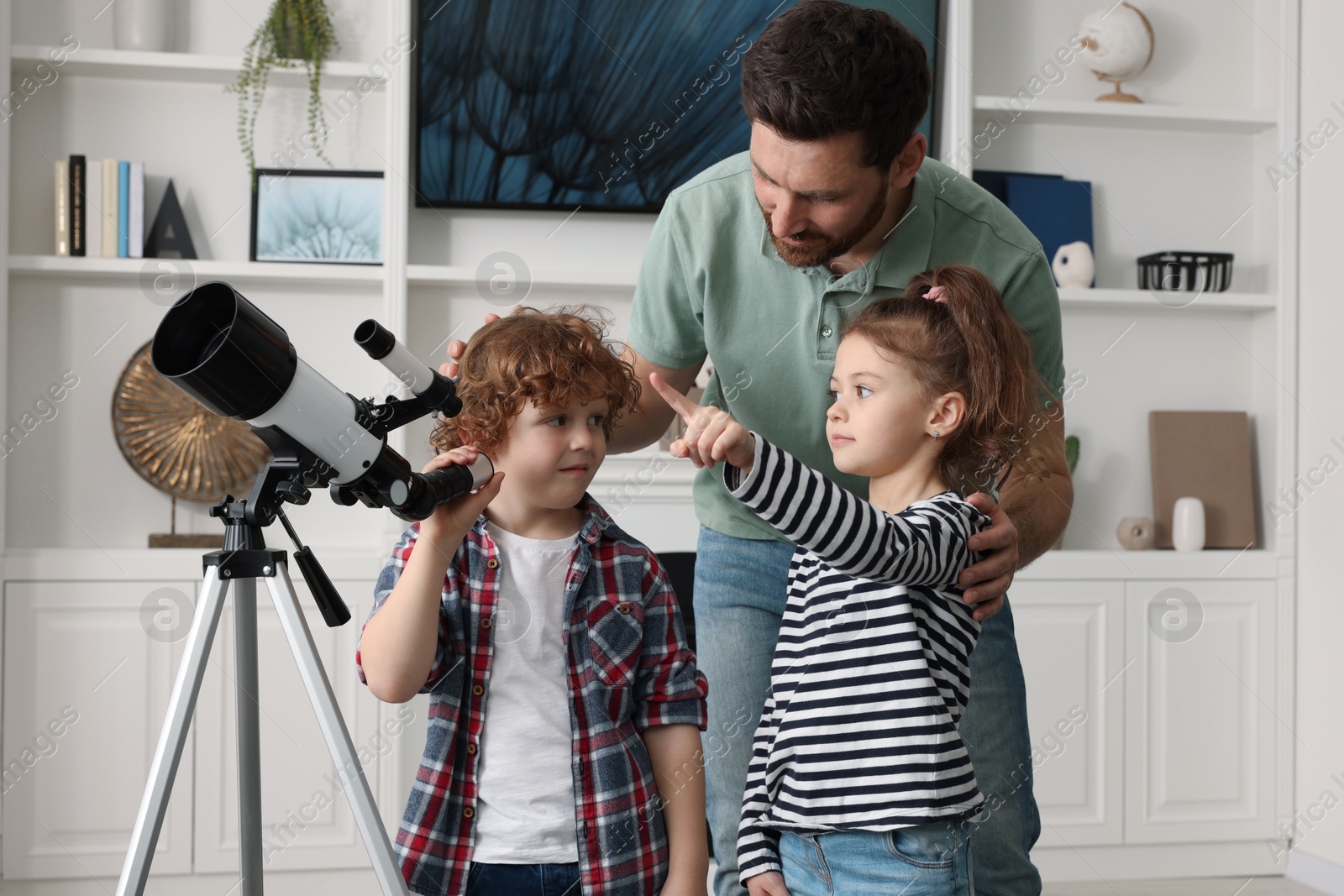 Photo of Happy father and children using telescope to look at stars in room