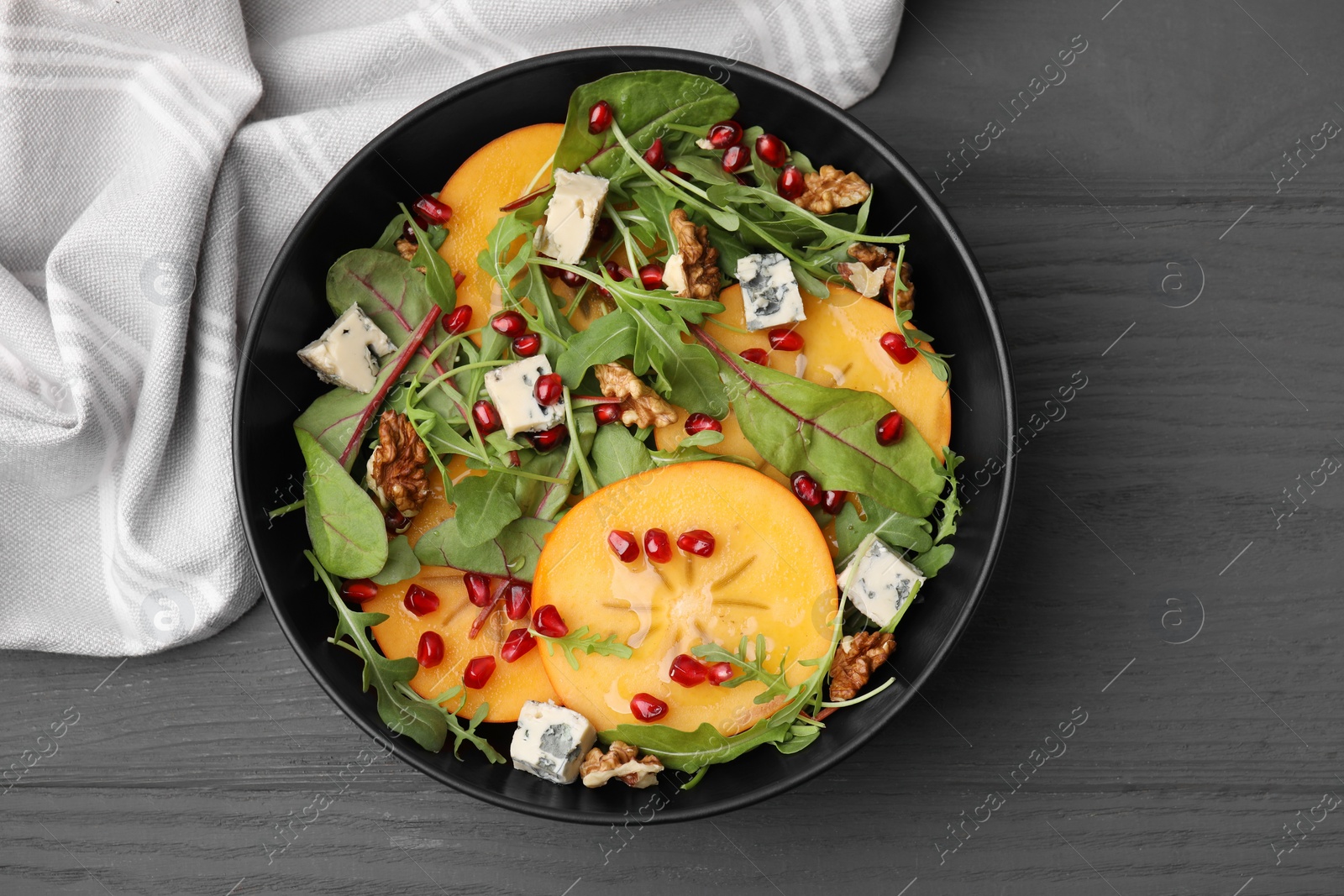 Photo of Tasty salad with persimmon, blue cheese, pomegranate and walnuts served on grey wooden table, top view