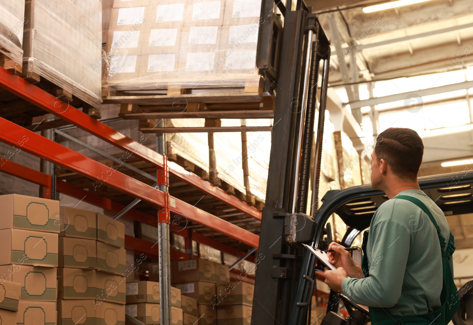 Image of Worker near forklift truck with cardboard boxes in warehouse. Logistics concept