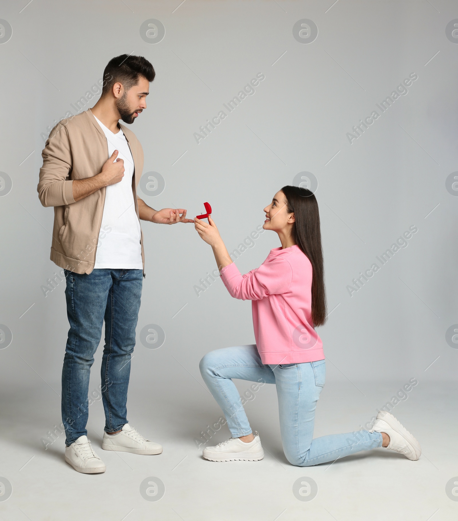 Photo of Young woman with engagement ring making marriage proposal to her boyfriend on light grey background