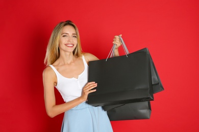 Photo of Happy young woman with shopping bags on red background. Black Friday Sale