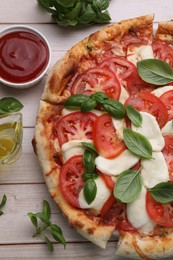 Photo of Delicious Caprese pizza with tomatoes, mozzarella and basil on light wooden table, flat lay