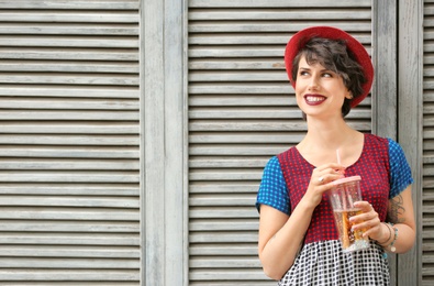 Young woman with cup of tasty lemonade near wooden wall