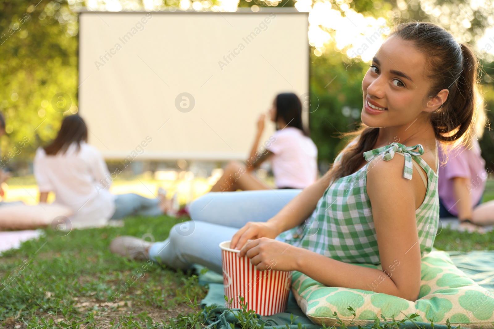 Photo of Young woman with popcorn watching movie in open air cinema. Space for text