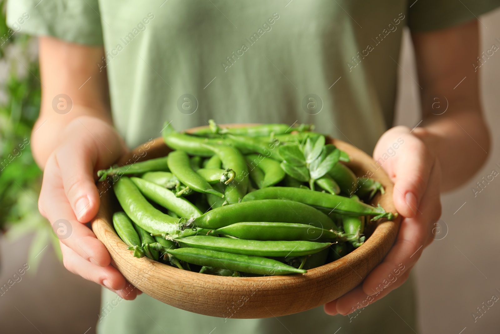 Photo of Young woman holding plate with green peas, closeup