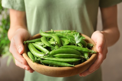 Photo of Young woman holding plate with green peas, closeup