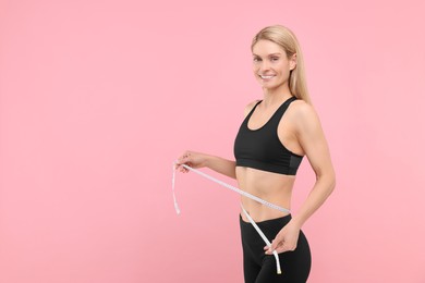 Photo of Slim woman measuring waist with tape on pink background, space for text. Weight loss