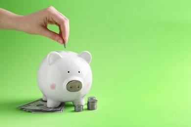 Financial savings. Woman putting coin into piggy bank on green background, closeup. Space for text