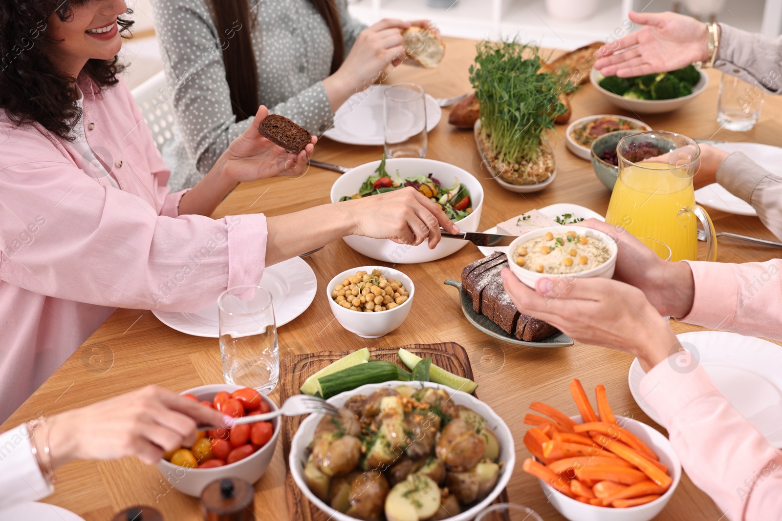 Photo of Friends eating vegetarian food at wooden table indoors, closeup