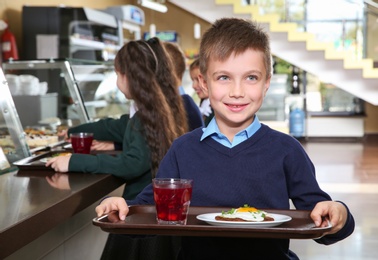 Photo of Cute boy holding tray with healthy food in school canteen