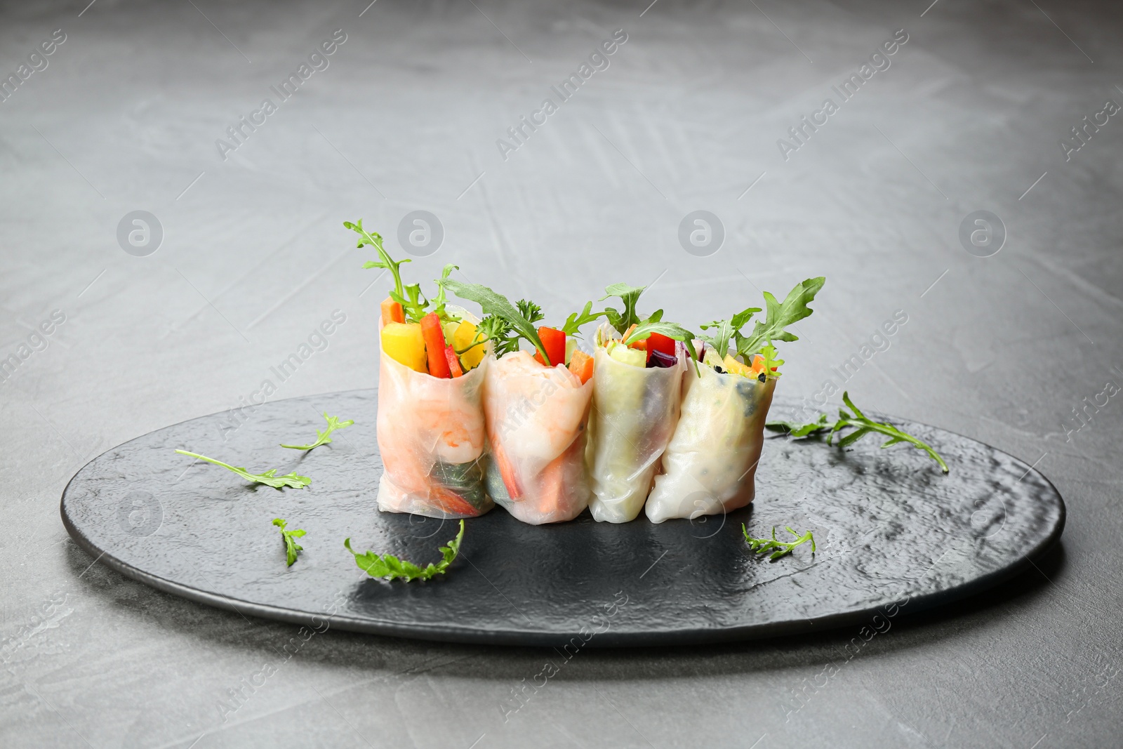 Photo of Delicious rolls wrapped in rice paper served on grey table