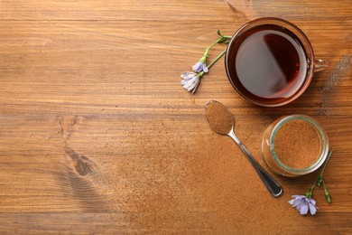 Cup of delicious chicory drink, powder and flowers on wooden table, flat lay. Space for text