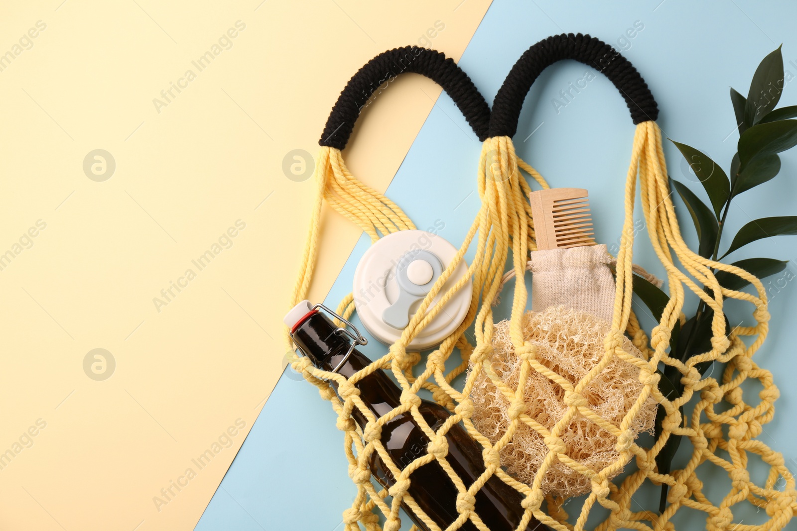 Photo of Fishnet bag with different items and green twig on color background, top view and space for text. Conscious consumption