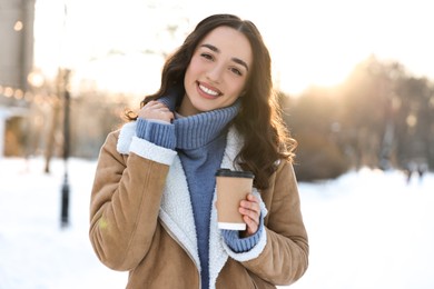 Photo of Portrait of smiling woman with paper cup of coffee in snowy park