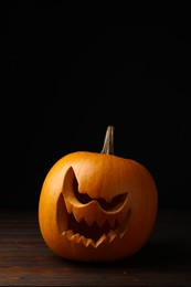 Scary jack o'lantern made of pumpkin on wooden table in darkness, space for text. Halloween traditional decor