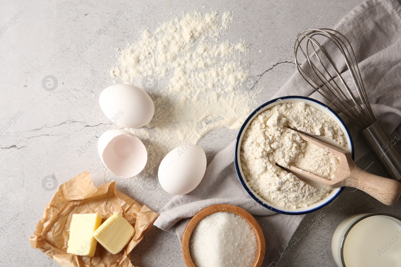 Photo of Different ingredients for dough and whisk on light textured table, flat lay