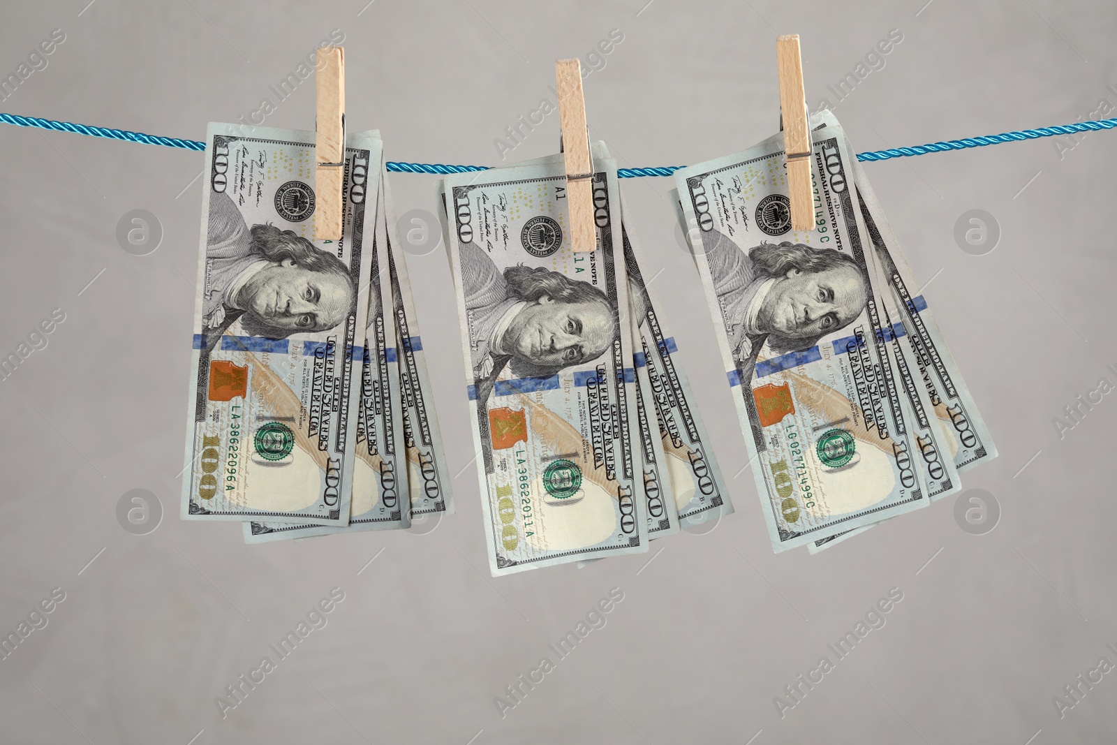 Photo of Dollar banknotes hanging on rope against light grey background